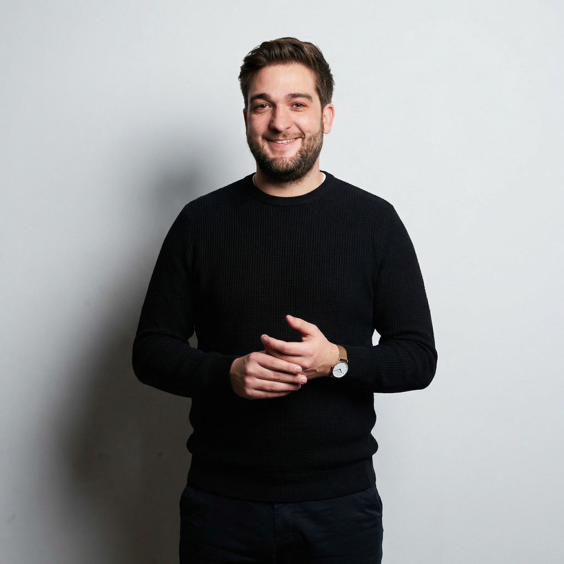 Portrait of Lloyd Palmer, founder of Obedient Minds — a smiling bearded man in a black knit jumper, hands clasped, photographed against a soft grey studio backdrop in London, 2025.